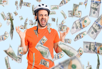 Young handsome man wearing bike helmet celebrating mad and crazy for success with arms raised and...