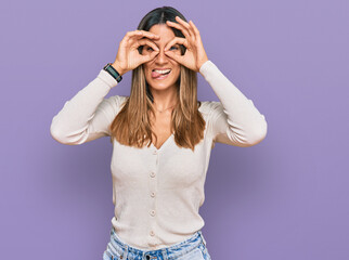 Young woman wearing casual clothes doing ok gesture like binoculars sticking tongue out, eyes looking through fingers. crazy expression.