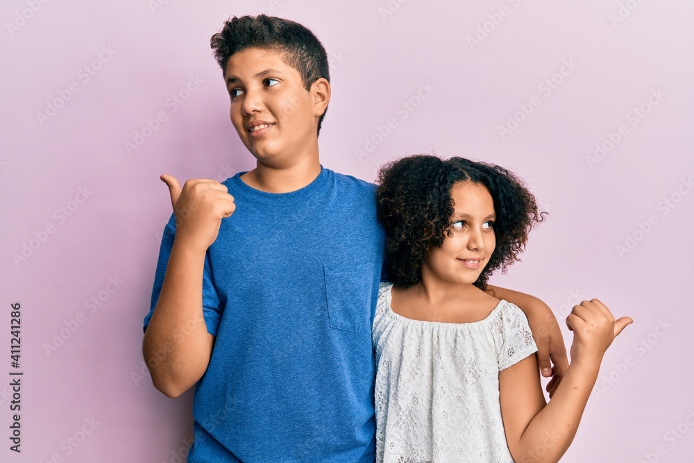 Poster Young hispanic family of brother and sister wearing casual clothes together smiling with happy face looking and pointing to the side with thumb up.