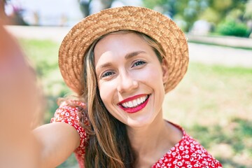 Young blonde woman on vacation smiling happy making selfie by the camera sitting on the park