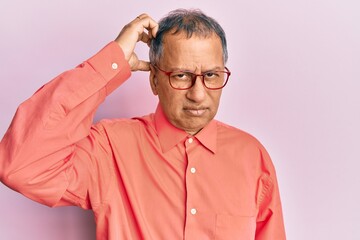 Fototapeta premium Middle age indian man wearing casual clothes and glasses confuse and wonder about question. uncertain with doubt, thinking with hand on head. pensive concept.