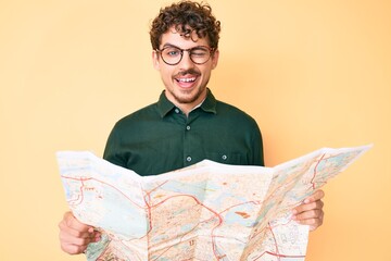 Young caucasian man with curly hair holding city map winking looking at the camera with sexy...