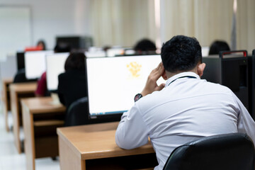 Blur and selective focus of the adult university learners wearing a face mask while concentrating on doing online examination in the computer room. Serious students working on computer at university