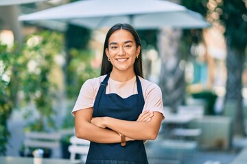 Young latin barista girl with arms crossed smiling happy at the coffee shop - obrazy, fototapety, plakaty