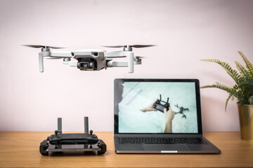 Learn how to fly drone flying in the air indoors safely with radio controller and laptop computer in the background out of focus showing tutorial guide on screen