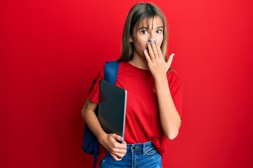 Teenager caucasian girl wearing student backpack and holding computer laptop covering mouth with...
