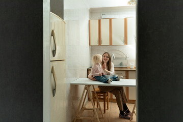 Fototapeta na wymiar Happy mom and child sitting in small kitchen. Evening atmosphere