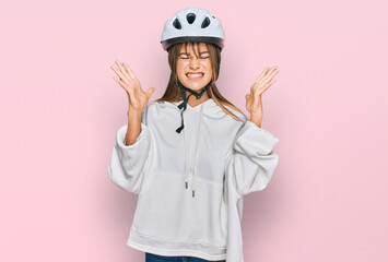 Teenager caucasian girl wearing bike helmet celebrating mad and crazy for success with arms raised and closed eyes screaming excited. winner concept