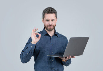 Computer programmer show ring gesture holding portable laptop grey background, OK