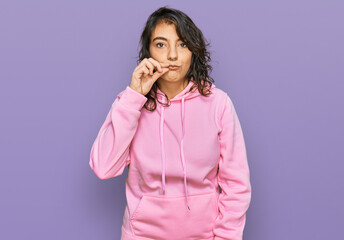 Young hispanic woman wearing casual sweatshirt mouth and lips shut as zip with fingers. secret and...
