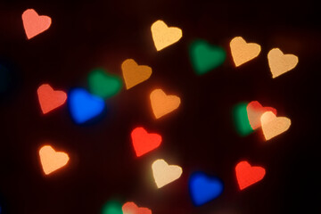 Bokeh in the shape of colorful hearts. Dark background.