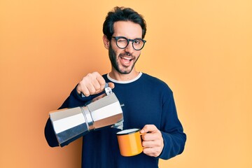 Young hispanic man drinking italian coffee winking looking at the camera with sexy expression,...