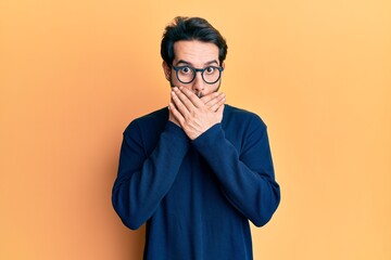 Young hispanic man wearing casual clothes and glasses shocked covering mouth with hands for...