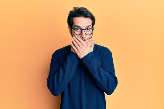 Young hispanic man wearing casual clothes and glasses shocked covering mouth with hands for mistake. secret concept.