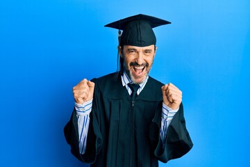 Middle age hispanic man wearing graduation cap and ceremony robe celebrating surprised and amazed for success with arms raised and open eyes. winner concept.