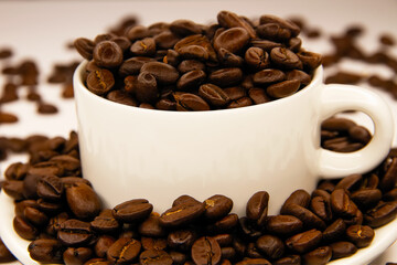A mug with coffee surrounded by coffee beans on a white background. Coffee beans in a coffee mug