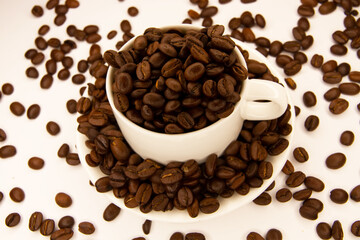 A mug with coffee surrounded by coffee beans on a white background. Coffee beans in a coffee mug