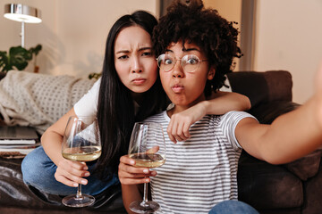 Two beautiful girls drink wine from beautiful glasses and take selfie