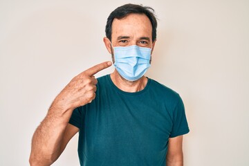 Middle age hispanic man wearing medical mask smiling happy pointing with hand and finger