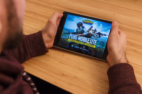 PRAGUE, CZECH REPUBLIC - MARCH 16, 2019: Man holding a smartphone and playng the PlayerUnknown s Battlegrounds PUBG mobile game. An illustrative editorial image on an bamboo background.