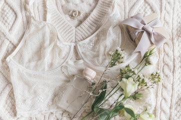 Stylish lingerie, perfume, modern jewelry and gift on sweater with spring flowers. Soft trendy image