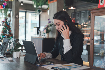 Asian businesswoman outside meeting at the bakery shop to use tablet and talking on the phone.