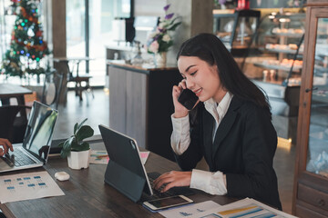 Asian businesswoman outside meeting at the bakery shop to use tablet and talking on the phone.