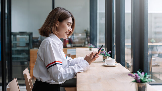 Image Side view of beautiful Asian woman look at their phone and drink coffee at a café.