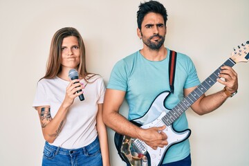 Beautiful young couple of boyfriend and girlfriend singing song using microphone and guitar skeptic...