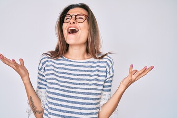 Beautiful caucasian woman wearing casual clothes and glasses crazy and mad shouting and yelling with aggressive expression and arms raised. frustration concept.