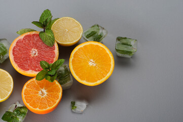 Cut in half fresh citrus fruits with mint and ice cubes on gray background. Citrus juice ingredients, food background. Preparation of drinks