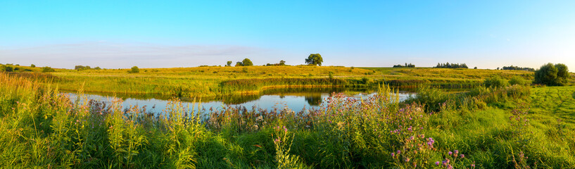 Fototapeta na wymiar Summer panoramic sunset landscape with calm river and green hills during sunny evening.