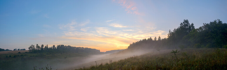 Beautiful summer hazy landscape with foggy hollow and green hills before the sunrise