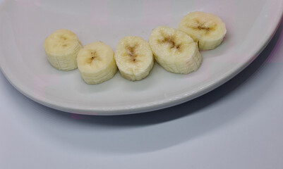 Five slices of banana laid out on a white plate on white background