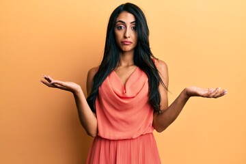 Beautiful hispanic woman wearing summer dress clueless and confused expression with arms and hands...