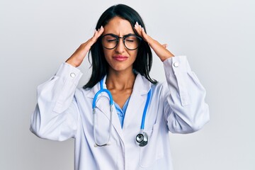 Beautiful hispanic woman wearing doctor uniform and stethoscope with hand on head, headache because stress. suffering migraine.