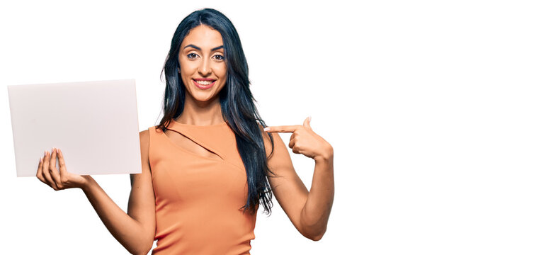 Beautiful hispanic woman holding blank empty banner pointing finger to one self smiling happy and proud