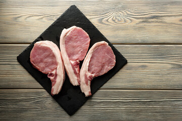 Flat lay composition with pieces of pork meat lying on a slate dish on a wooden table with copy space.