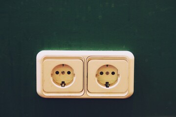 Enchufe en una pared verde. Enchufe doble antiguo con el sistema de clavijas español en Madrid.