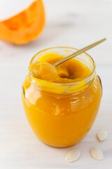 Pumpkin jam with a spoon in a glass jar.