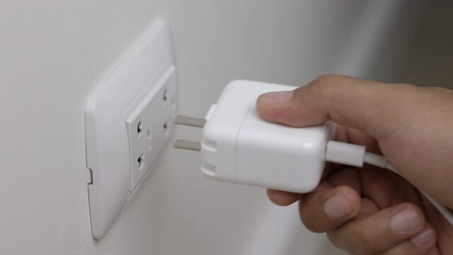 Close up male hand put on the Electric adapter smartphone or laptop plug. Electrical wires and power strips in the house