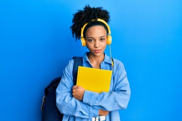 Young african american girl wearing student backpack and headphones holding book skeptic and nervous, frowning upset because of problem. negative person.