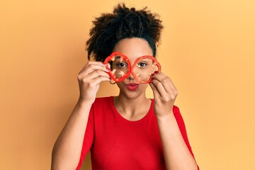 Young african american girl holding red pepper as a glasses looking at the camera blowing a kiss being lovely and sexy. love expression.