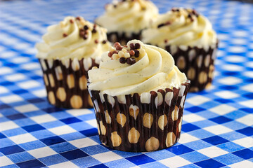 Sweet Cakes is a close up color image of frosted cup cakes on a blue and white tablecloth.