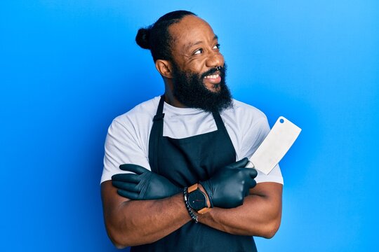 Young african american man wearing professional apron holding knife smiling looking to the side and staring away thinking.