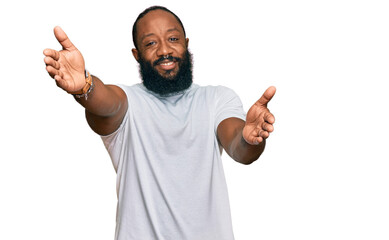 Young african american man wearing casual white tshirt looking at the camera smiling with open arms for hug. cheerful expression embracing happiness.