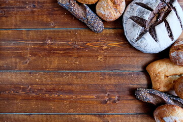 Freshly baked bread of various shapes lies on a brown wooden surface.Copy space. Top view.