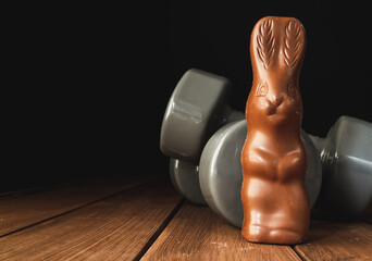 Chocolate Easter bunny with heavy dumbbells on wooden table. Easter fitness and training...
