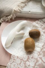 white silicone vibrator with vacuum mode on pink lace background with kiwi on the plat
