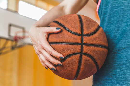 Female high school basketball player holding a ball on school gymnasium, with basketball board in background.